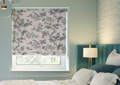 a bedroom with blue walls and white bedding has a pink floral roman blind in the window