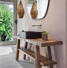 a bathroom sink sitting under a mirror next to a wooden bench with a potted plant on it