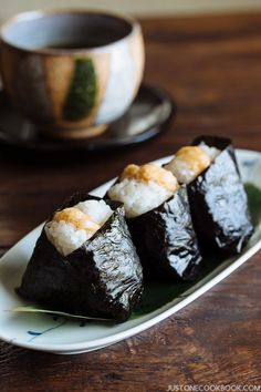 three sushi rolls on a plate next to a cup of coffee