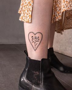 a woman's leg with a small heart and flowers tattoo on her left ankle