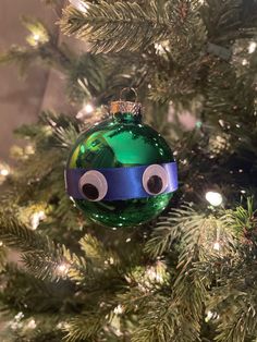 a green ornament hanging from the side of a christmas tree with eyes drawn on it