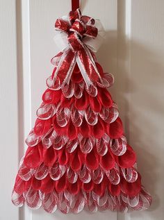 a red and white christmas tree hanging from a door with ribbon on the top,