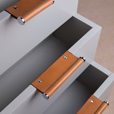 two brown leather drawers with metal handles on each side and one drawer open to show the inside