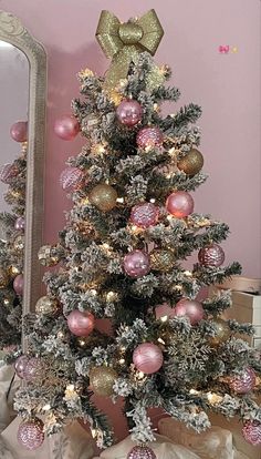 a small christmas tree with pink and gold ornaments on it in front of a mirror