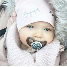 a baby wearing a pink hat with eyelashes on it's face and a pacifier in its mouth