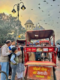 a group of people standing next to a red cart with birds flying over the top