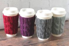 four knitted coffee cups sitting next to each other on top of a wooden table