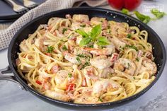 a skillet filled with pasta and meat on top of a white countertop next to tomatoes