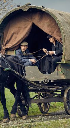 two men riding in a covered wagon being pulled by a horse