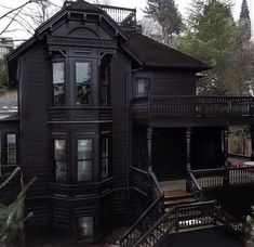 an old black house in the middle of some trees and houses with balconies