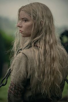 a woman with long hair standing in front of a green field and looking off into the distance