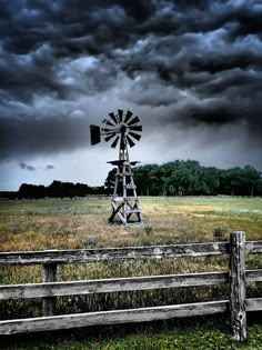 a windmill sitting in the middle of a field next to a wooden fence under a cloudy sky