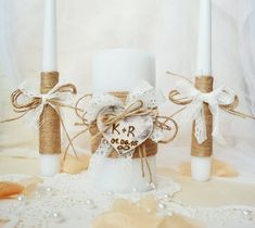 three white candles are sitting next to each other on a lace tablecloth with burlocks and twine