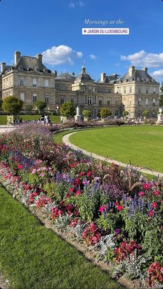 a large building sitting next to a lush green field filled with purple and red flowers