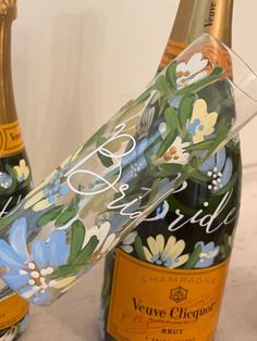 two champagne bottles with floral designs on them and one has a wine glass in front of it