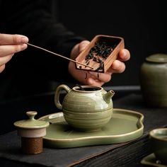 a person is holding a small teapot and stirring it with a wooden stick in their hand