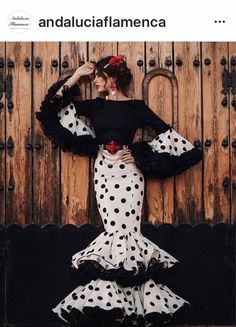 a woman in a black top and white polka dot skirt is leaning against a wooden door