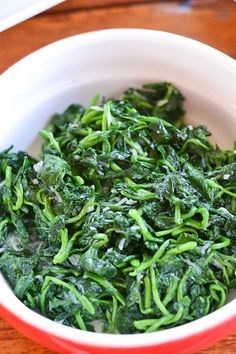 a white bowl filled with greens on top of a wooden table