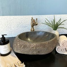 a black counter top with a stone sink and towels on it next to a potted plant