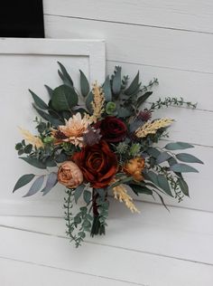 a bouquet of flowers sitting on the side of a white door with greenery and leaves