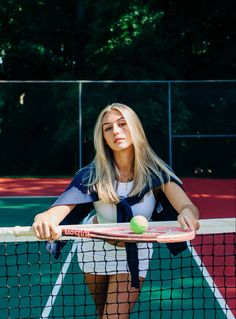 a woman holding a tennis racquet on top of a tennis court next to a net