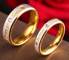 two gold wedding rings with the word love written on each side and diamonds in between them