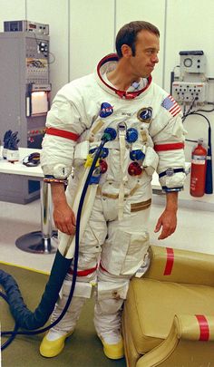 a man in an astronaut's suit standing next to a couch with a hose attached to it