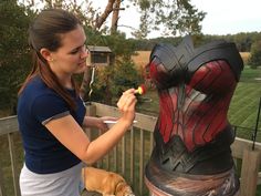 a woman is painting a statue on a deck with a dog nearby in the foreground