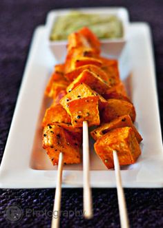 skewers of tofu on a white plate with dipping sauce in the background