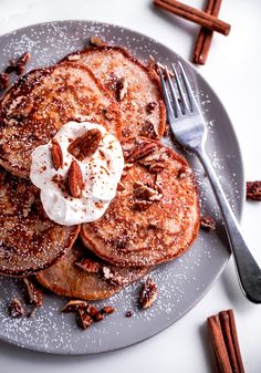 a plate topped with pancakes covered in whipped cream and pecans next to cinnamon sticks