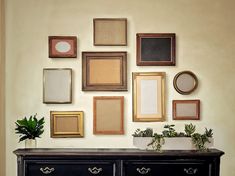 a black dresser topped with lots of framed pictures next to a wall filled with potted plants