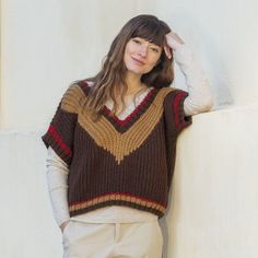 a woman leaning against a wall with her hand on her head and wearing a sweater