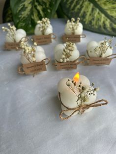 small white candles are sitting on a table with some tags around them that have flowers in them