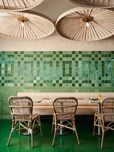 the interior of a restaurant with wicker chairs and green tiled walls, along with bamboo umbrellas hanging from the ceiling