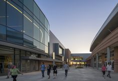 several people are walking down the street in front of some buildings at sunset or dawn