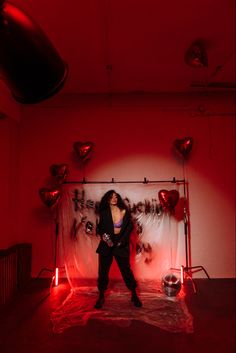 a woman standing in front of a red backdrop with heart shaped balloons on the wall