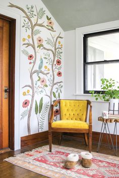 a yellow chair sitting on top of a rug in front of a tree wall mural