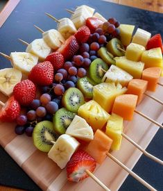 fruit skewers are arranged on a cutting board with strawberries, grapes and kiwis