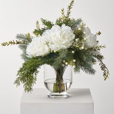 a glass vase filled with white flowers and greenery