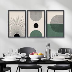 three paintings hang above a dining room table with plates and glasses on it, along with bowls of fruit