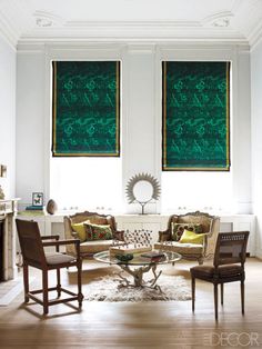 a living room filled with furniture and two large windows covered in green drapes