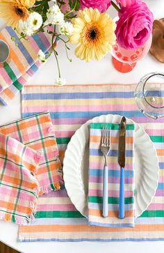 a place setting with colorful napkins, flowers and utensils on the table