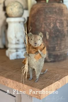 a toy mouse is standing on top of a wooden table holding a piece of hay