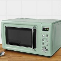 a green microwave oven sitting on top of a wooden table next to a silver spoon