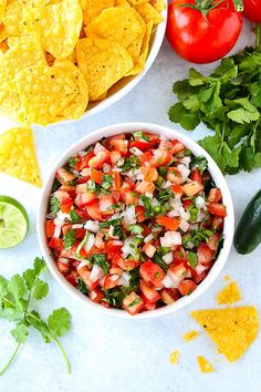 a white bowl filled with salsa surrounded by tortilla chips, tomatoes and cilantro