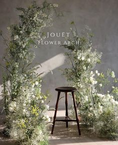 a stool sitting in front of a flower arch with white flowers and greenery around it