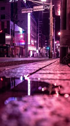 a city street at night with lights reflecting in the puddles on the pavement and buildings