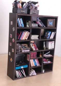 a book shelf with many books and other items in it on top of a wooden table