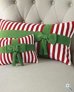 two red and white striped pillows with green bows on them sitting on a couch next to each other