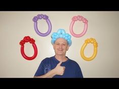 an older man with balloons on his head gives the thumbs up in front of him